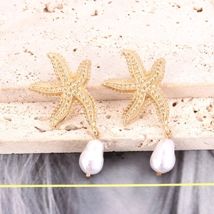 Détail de boucles d'oreilles étoile de mer dorées avec surface texturée et perles baroques