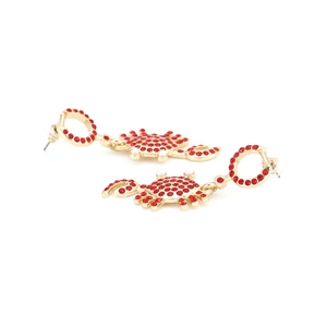 Détail de boucles d'oreilles crabe dorées avec strass rouges et perles blanches sur fond blanc