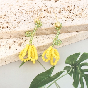 Detail shot of handmade flower earrings featuring yellow beads and green stems on travertine
