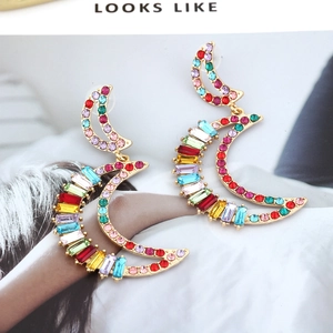 Close-up of golden crescent earrings with vibrant colorful rhinestones on a fashion background
