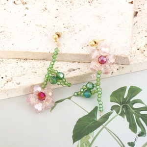 Detail of handmade beaded flower earrings featuring pink crystal petals and green leaves