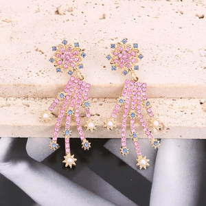 Detail view of gold starburst earrings with pink crystals and long pearl tassel chains