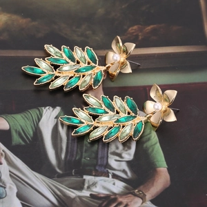 Macro detail of vintage gold leaf earrings with green crystals and pearl floral accents