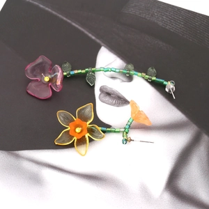 Macro shot of asymmetric resin flower earrings with green beaded vines on artistic background
