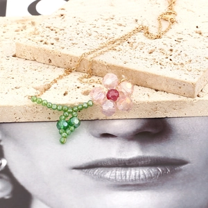 Detail view of handcrafted pink crystal flower pendant with green beaded leaf on gold chain