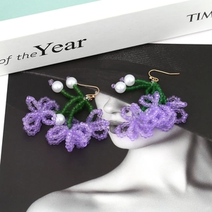 Handmade beaded flower tassel earrings with purple and green floral design on a magazine