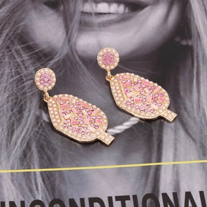 Macro shot of gold-plated shield earrings with pink crystals and pearls on a magazine