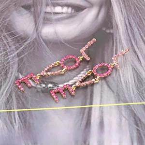 Detailed macro view of long LOVE drop earrings with pink rhinestones on a gold alloy base