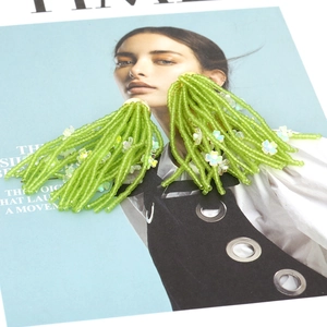 Green beaded fringe earrings with flower accents and golden studs on magazine background