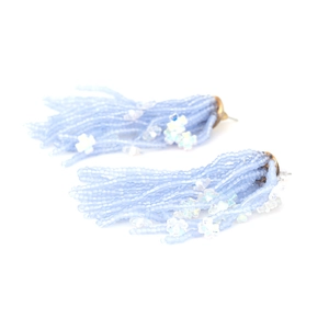Detail of handmade light blue beaded tassel earrings with small white flower accent