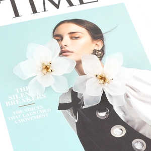Detail of white resin floral earrings with gold centers on a fashion magazine