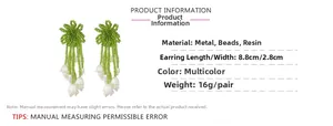 Détail de boucles d'oreilles en perles vertes faites main avec muguet en résine blanche