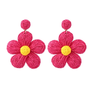 Macro view of woven raffia flower earrings showing pink petals and yellow core detail