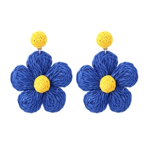 Macro detail of hand-woven raffia flower earrings in navy blue and yellow bohemian style