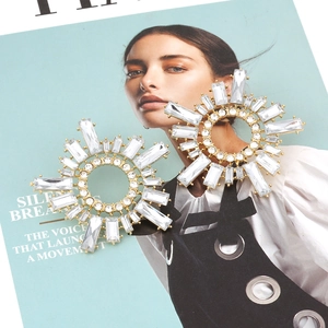 Detailed view of large golden sunburst earrings with clear baguette crystals on a magazine