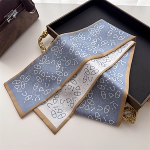 Detail of luxury narrow silk scarf with H-pattern print and gold trim on black tray