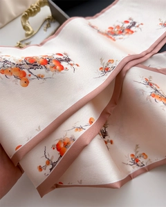 Detail of silk scarf with orange persimmon print and elegant pink edge over black tray