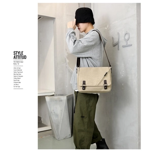 Detail view of beige canvas messenger bag with brown leather straps and metal buckle