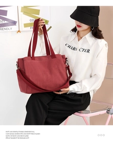 Deep red canvas tote bag with dual handles and wide shoulder strap shown on a model
