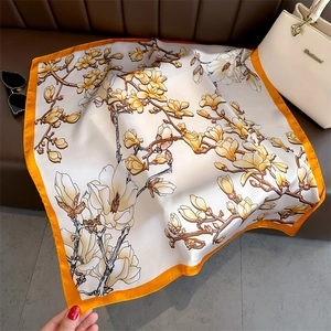 Floral magnolia print satin silk square scarf with orange borders on leather surface