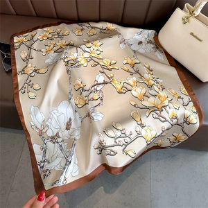 Detail of silk square scarf with magnolia print and brown border on a leather sofa