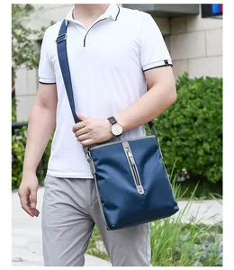 Detail view of the large navy blue Oxford fabric messenger bag worn by a model outdoors