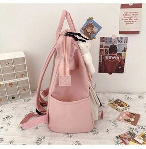Side view of pink and white school backpack with cute plush bear charm on a desk