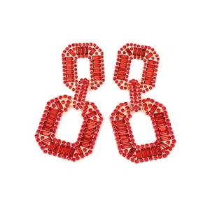 Macro detail of geometric gold earrings featuring red rhinestones and crystal pavé