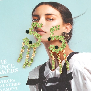 Elegant gold earrings with light green rhinestones and tassel fringe on magazine background