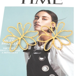 Gros plan de grandes boucles d'oreilles fleurs dorées mates avec texture martelée sur revue