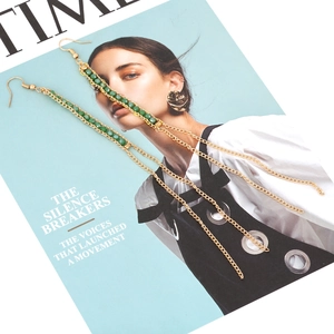 Boucles d'oreilles longues à pompon doré avec perles vertes sur fond de magazine