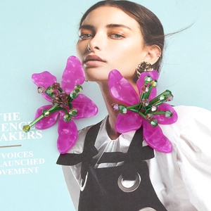 Statement purple acrylic flower earrings with green beaded center on fashion magazine