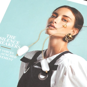 Long gold tassel earrings featuring large white baroque pearls on a fashion magazine
