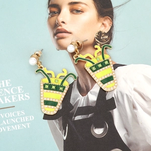 Detail of drink cup earrings with yellow-green enamel and pearl accents on magazine backdrop