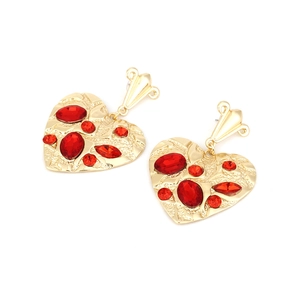 Macro detail of vintage heart earrings with hammered gold finish and red gemstones