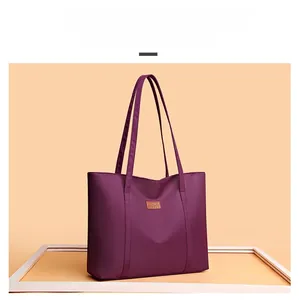 Detail view of purple trapezoid nylon tote bag with long shoulder straps and logo