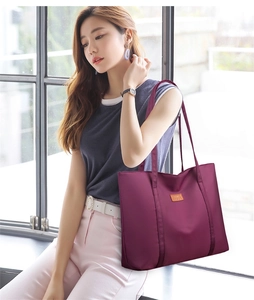 Detail of a large purple nylon tote bag with dual straps and a brown leather NICE logo