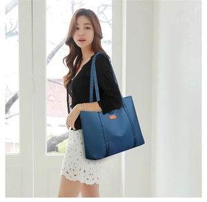 Detail of navy nylon tote bag with orange logo patch worn in a bright indoor setting