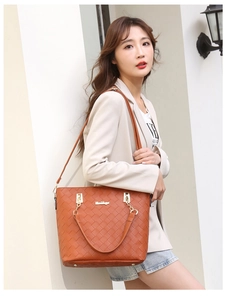 Detail of caramel woven tote bag with metallic logo and chain shoulder strap on model