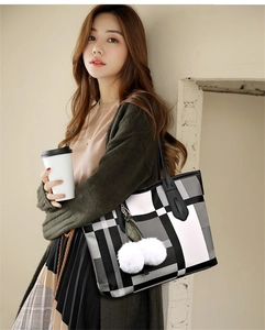Macro detail of geometric checkered tote bag with white pom-pom charms and shoulder straps