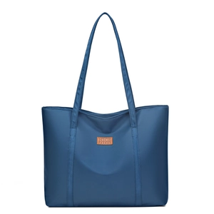 Minimalist navy blue nylon tote bag with brown leather logo patch on white background