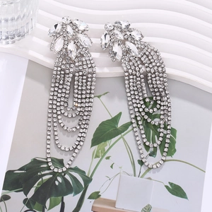 Detailed close-up of sparkling rhinestone tassel earrings on elegant white wave pedestal