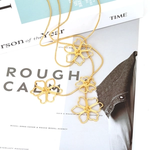 Detail of long gold chain necklace featuring four hollow floral pendants on a magazine