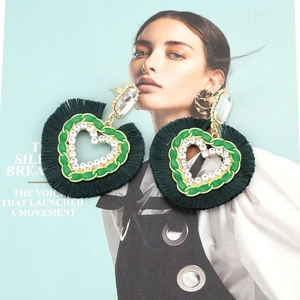 Green heart tassel earrings with rhinestone accents on a stylish magazine backdrop