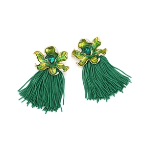 Macro detail of gold-tone floral earrings with green enamel petals and long silk tassels