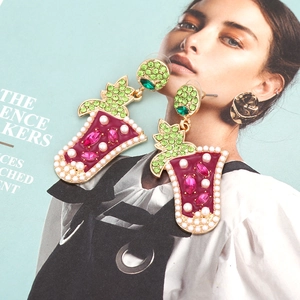 Orecchini creativi a forma di cocktail con strass colorati e perle su sfondo di rivista