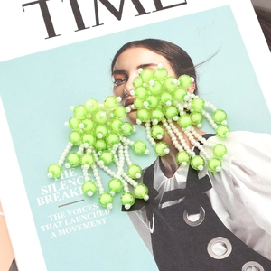 Close-up of handmade green beaded fringe earrings with white pearl floral details