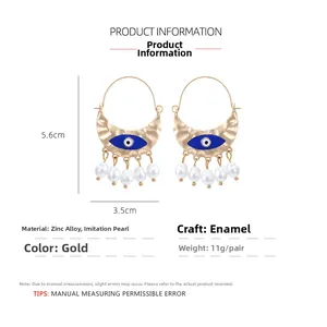 Detail of gold evil eye earrings with enamel finish and five white hanging pearls