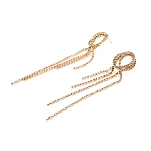 Détail de longues boucles d'oreilles dorées à glands avec strass brillants et nœud