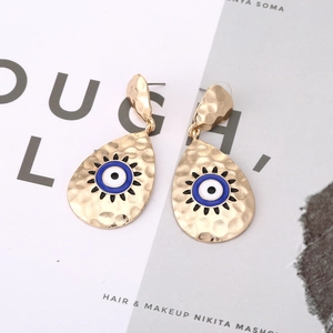 Retro goldene Tropfenohrringe mit blauem Emaille-Auge auf künstlerischem Hintergrund